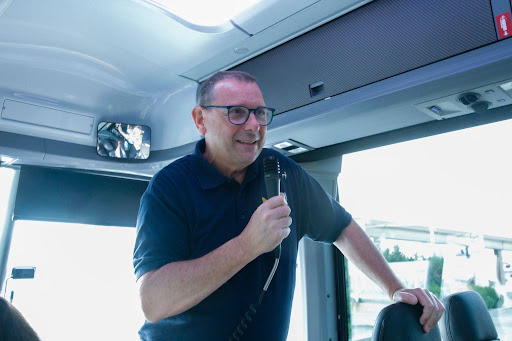 Andrew Donaldson speaks at the front of a bus with a microphone in his hand